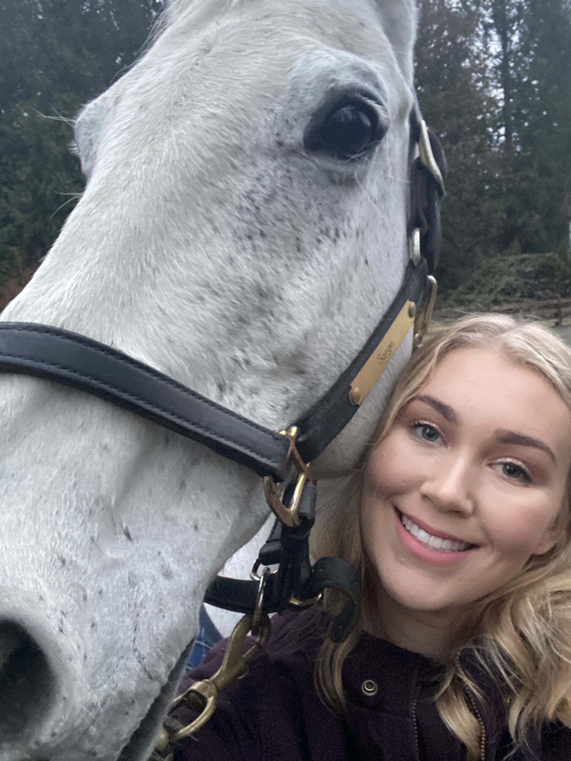 Tia Anderson standing with a grey horse in the barn aisle